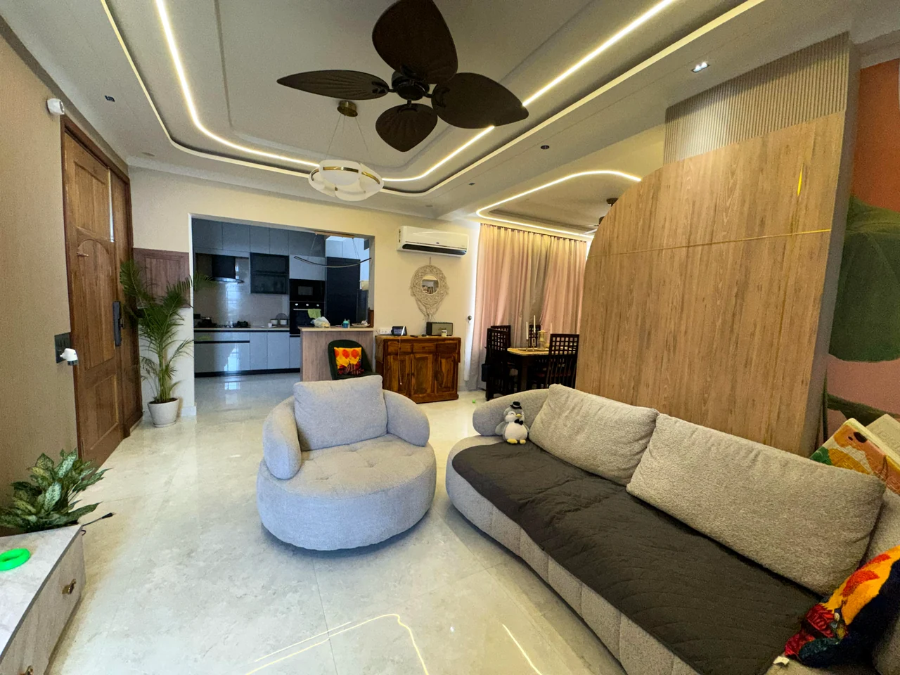 Open-plan living and dining interior with curved seating, timber partition and connected kitchen at TDI Wellington, Sector 117, Mohali